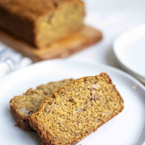two slices of whole wheat sourdough banana bread on a plate with the rest of the loaf in the background.