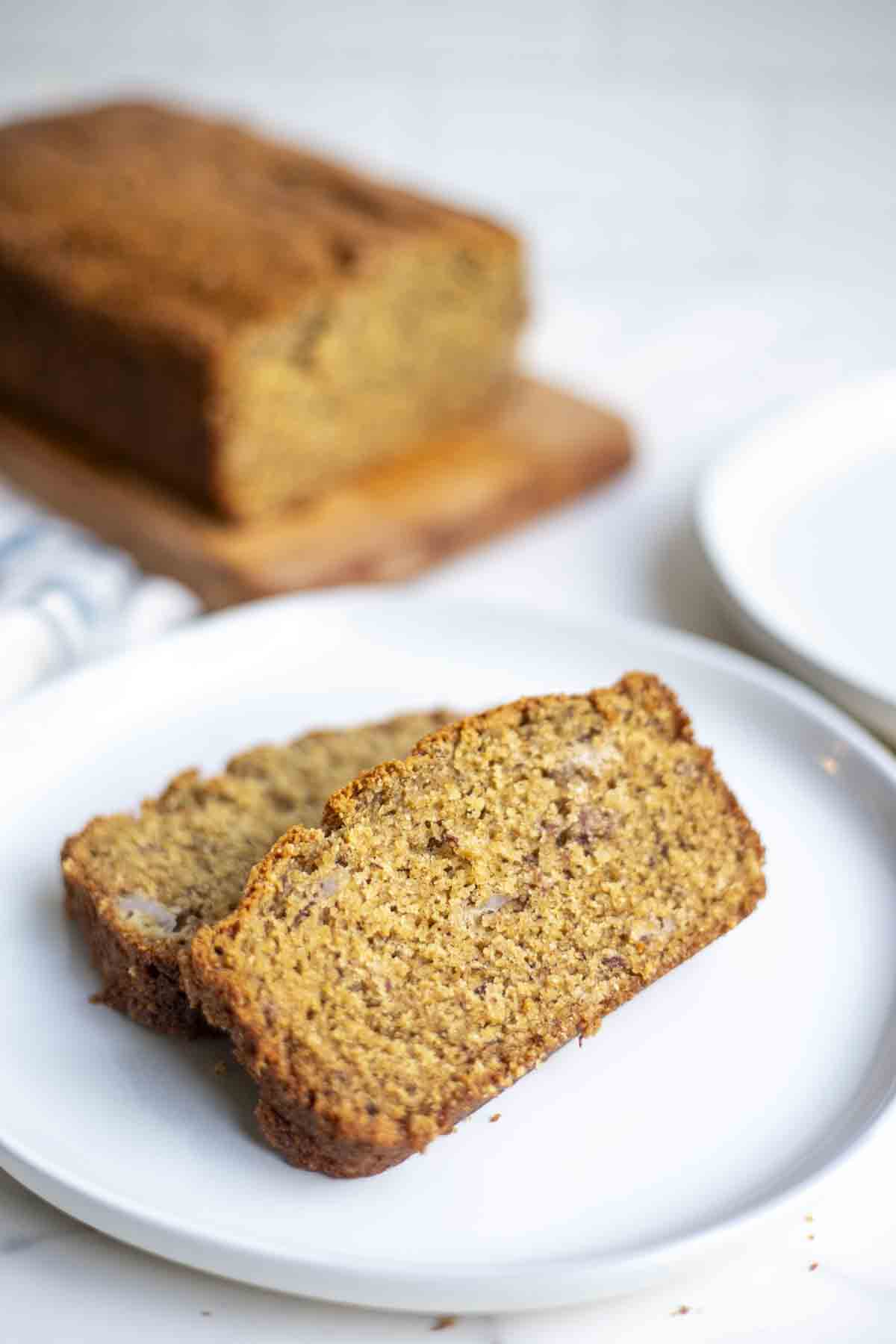 two slices of whole wheat sourdough banana bread on a plate with the rest of the loaf in the background.