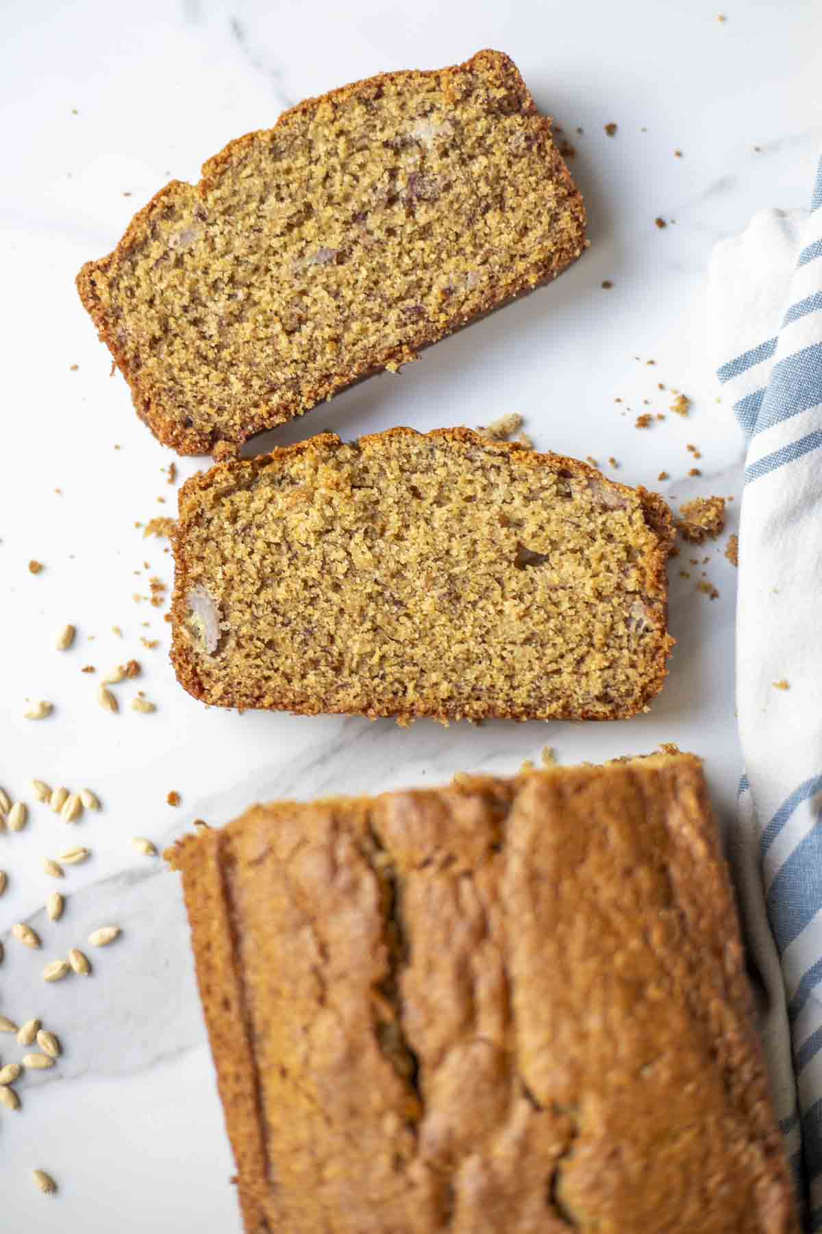 sliced sourdough banana bread on a countertop with wheat berries spread out on the countertop.