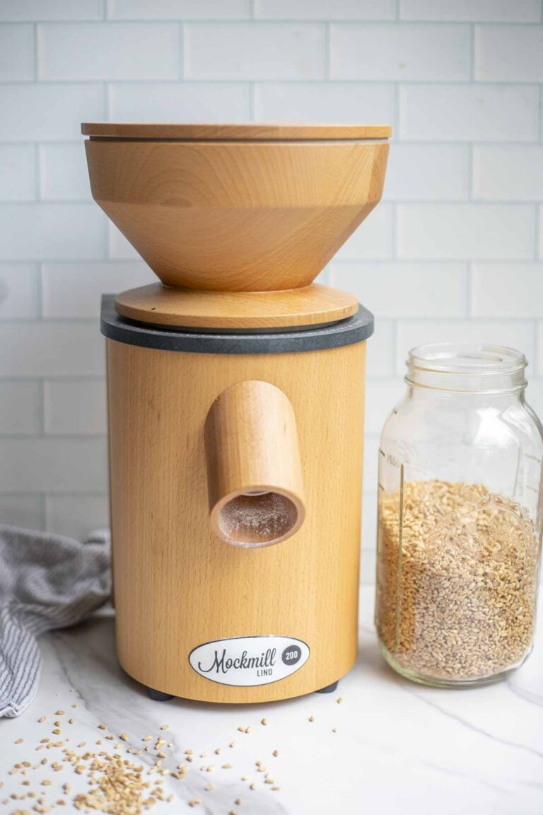 Mockmill grain mill next to a jar of wheat berries on a marble countertop.