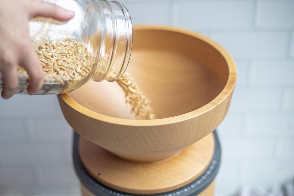 pouring wheat berries into the hopper of a grain mill.