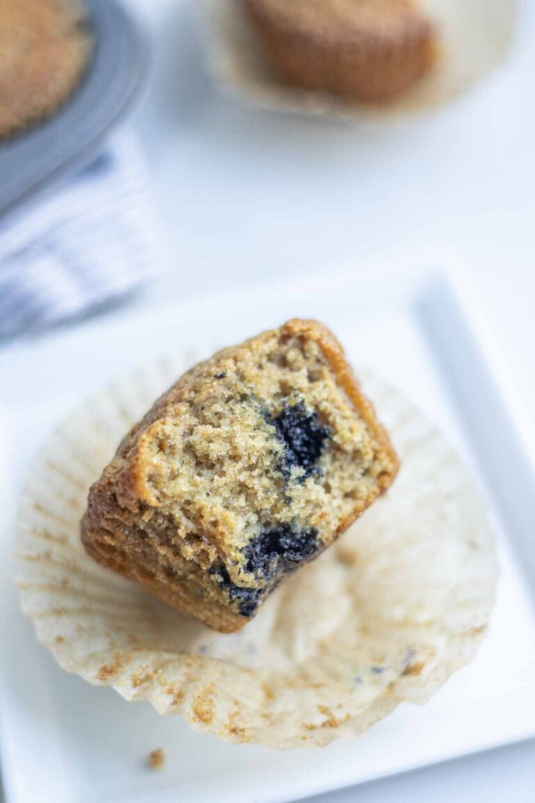 a half of a whole grain sourdough blueberry muffin on a white plate.