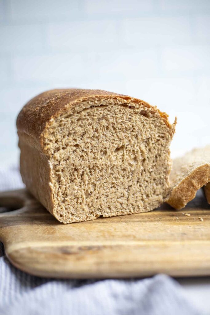 half a loaf of whole wheat sourdough sandwich bread on a wood cutting board.